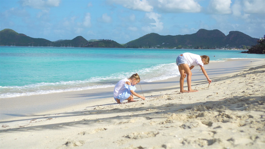 两个快乐的小女孩在热带沙滩玩沙子玩得开心极了视频