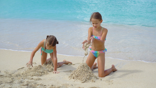 两个快乐的小女孩在热带海滩玩得很开心在浅水里玩耍孩子视频
