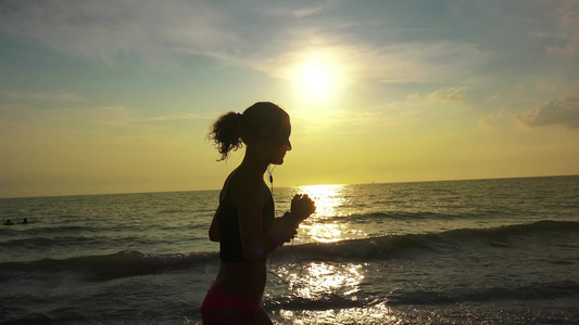 穿着马尾和耳机的跑漂亮女孩在夏季海滩日落时放松慢跑视频