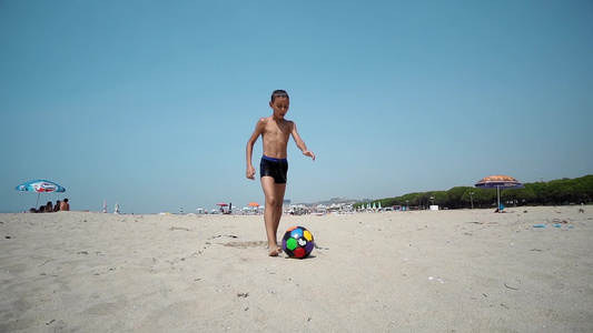 快乐的孩子踢足球赤脚跑在湿沙沙滩上踢球缓慢运动电影视频