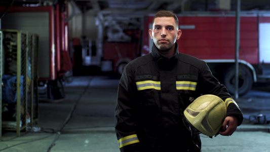 消防员视频肖像身着制服手持黄色防护头盔背景中的消防车视频