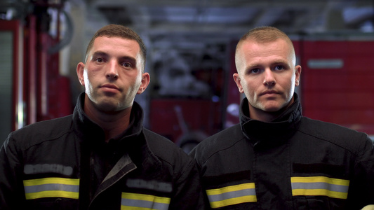 两名消防员站在一起身着制服手持黄色保护头盔近距离肖像视频