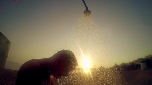 男子在沙滩上露天洗澡在日落和缓慢运动的光照下视频