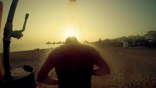 男子在沙滩上露天洗澡在日落和缓慢运动的光照下视频
