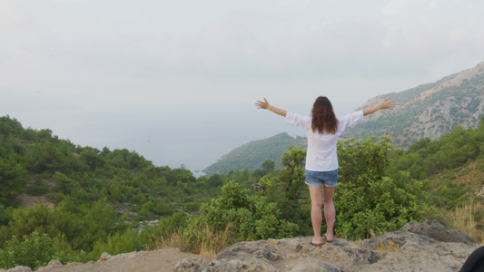 旅游女人站在山边伸出双手旅行的女人在青山景观上举手视频