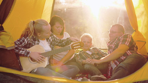 旅游家庭在阳光明媚的露营帐篷内休息和弹奏吉他30秒视频