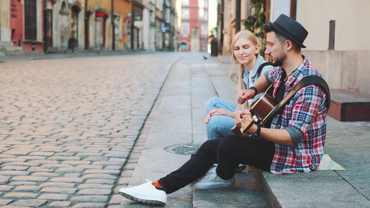 男人和女人坐在人行道上弹吉他和休息视频