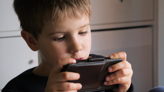 男孩在智能手机上玩手机游戏学龄前儿童玩手机孩子用手机视频