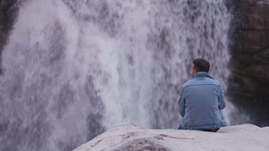 年轻印度男子坐在岩石上看瀑布18秒视频