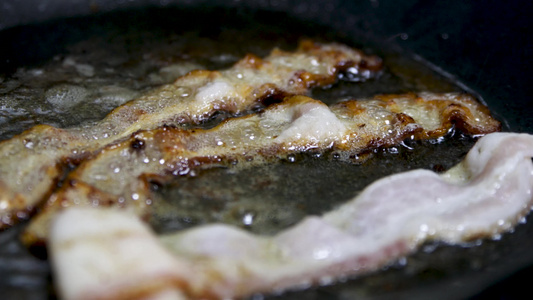 用大量油在平底锅中煎炸的香脆培根片的特写镜头猪肉培根视频
