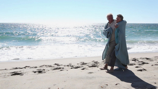 裹着毯子在沙滩上散步的成熟夫妇视频