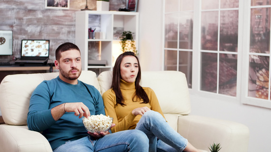 年轻夫妇笑着看着电视坐在沙发上视频