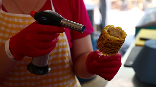 妇女用煤气火炬在棍子上煮玉米鳕鱼视频