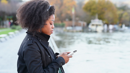 卷发女子站在河边智能手机回消息视频