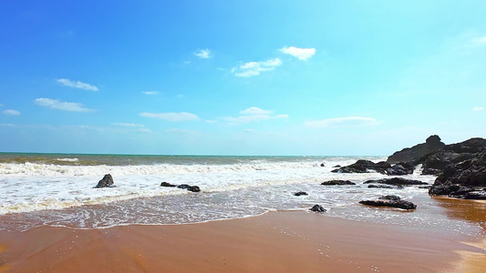海南省万宁市山钦湾蓝天白云下金色沙滩上汹涌奔腾的海浪浪花视频