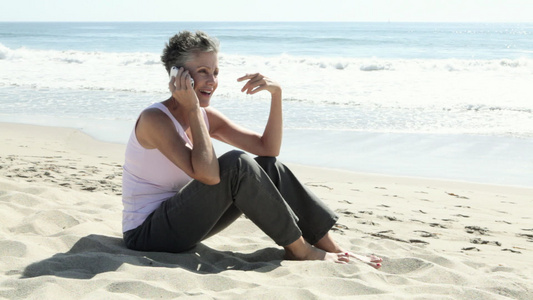 在海滩上使用手机的高级女性视频