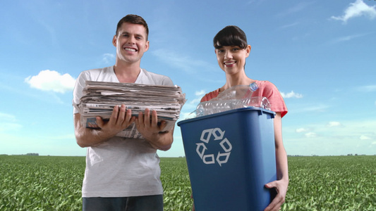 一对夫妇在田野里拿着回收箱和一堆报纸视频