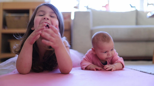 小女孩笑着躺在她小妹妹旁边,坐在粉红色地毯上视频