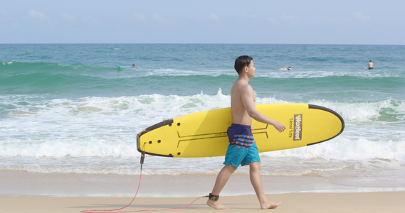 8K男青年抱着冲浪板走在沙滩上视频