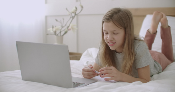 快乐的女学生通过笔记本电脑在网上课程中回答躺在床上视频