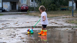 一个穿着橙色靴子的孩子拉着玩具在雨后走过水坑12秒视频