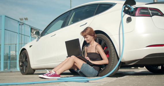 女孩在电动车充电时在地上等着用笔记本电脑工作视频