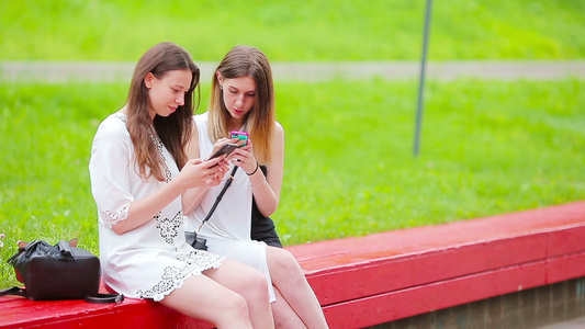 两名女孩在户外使用智能手机两名妇女坐在公园里用智能视频