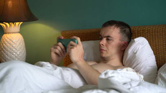 男人躺在床上正在用智能手机使用申请表笑声视频