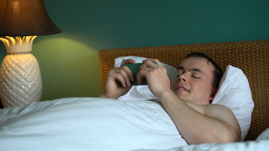 男人躺在床上正在用智能手机使用申请表笑声视频