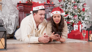 使用智能手机圣诞节装饰室在网上买地上笑着的情侣坐在16秒视频