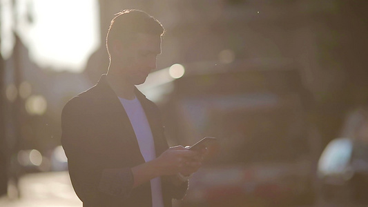 青年男子在街上使用软光的手机户外行动电话视频