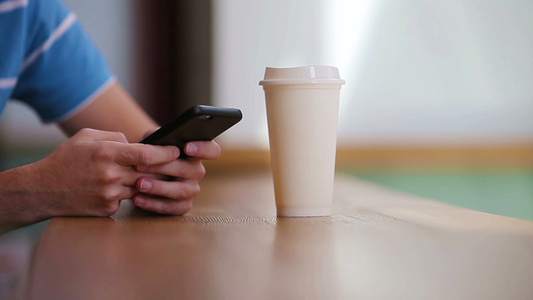 在咖啡馆里拿着手机和一杯咖啡的男性手的特写使用移动视频