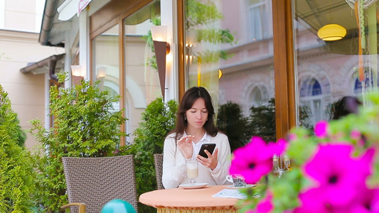 喝杯咖啡的年轻女孩使用智能手机在户外咖啡馆自拍散步视频