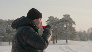 成年男子在冬季的雪地森林上喝热茶21秒视频
