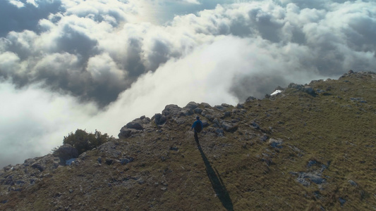 有背包的徒步男子正在行走站在云端高地的陡峭边缘举起手来视频