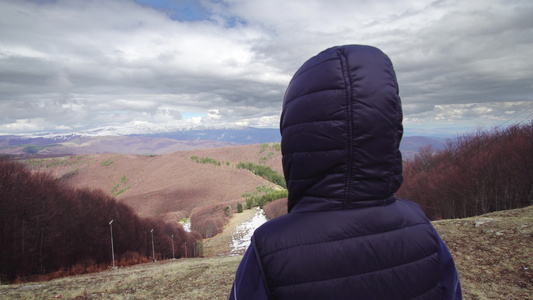 戴着帽子和黑客帽的男孩站在山顶上看着惊人的风景视频