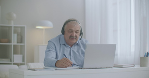 中年男子使用笔记本电脑和耳机与在家的同事和雇员通过17秒视频