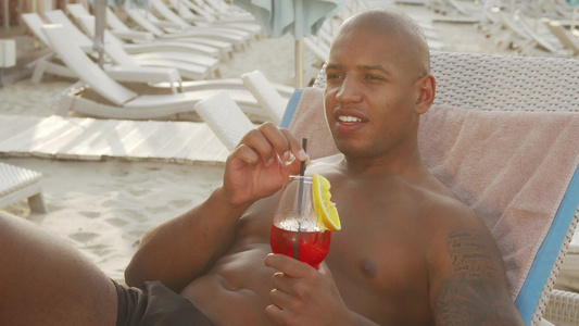 英俊的非洲男人在沙滩上放松时喝鸡尾酒视频
