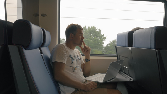 年轻男子在火车上乘车和手持笔记本电脑在桌子上对着窗户视频