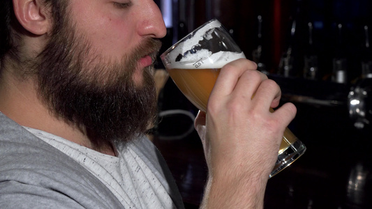 在酒吧喝着美味的啤酒后长胡子的男人笑着视频