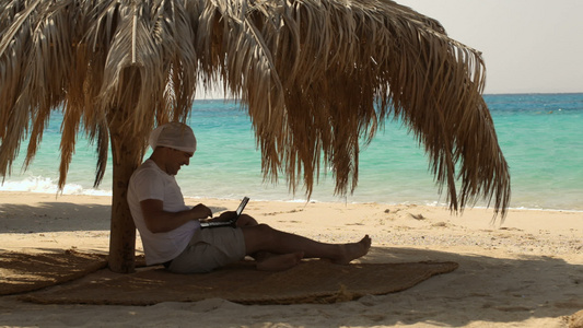 男人在海滩上用笔记本电脑视频