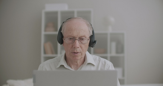 戴耳机的老人正在说话看着笔记本的显示屏在家在线讲课视频
