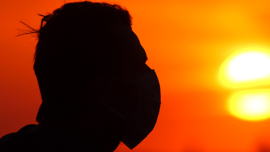戴外科防护面罩的男性肖像侧视图在美丽的日落日出背景视频