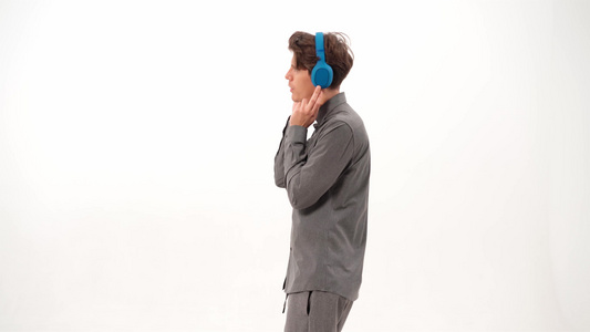 穿着灰色运动服的英俊年轻人戴着蓝色无线耳机跳舞听音乐视频