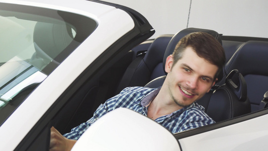 坐在汽车里拿着车钥匙的年轻男子驾驶员长着英俊快乐的视频