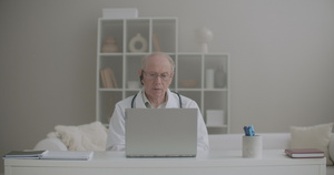 老年男性医生在门诊部的办公室远程工作使用笔记本电脑20秒视频