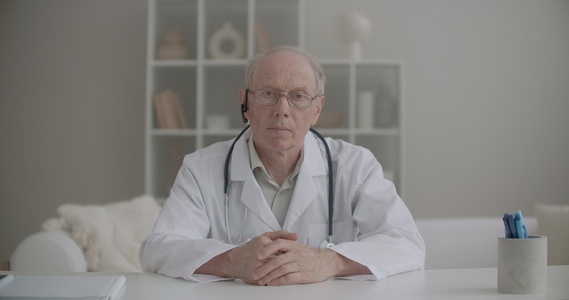 老年男医生坐在诊所里在线视频聊天点头视频会议时听视频