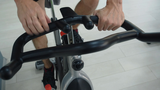 男性手在健身俱乐部握着手柄静态自行车运动员在健身房视频