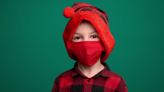 穿着圣塔帽的小男孩的肖像戴着红色医疗面具看着摄像机视频