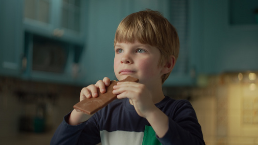 金发学龄前男孩的肖像喜欢吃巧克力棒站在蓝色的厨房孩子视频